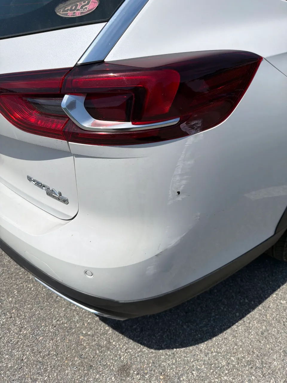 White Buick before repair, with a dented and scuffed rear bumper corner below the taillight